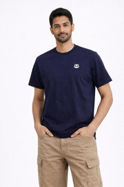 Man wearing a navy blue t-shirt with a small logo and beige pants on a white background